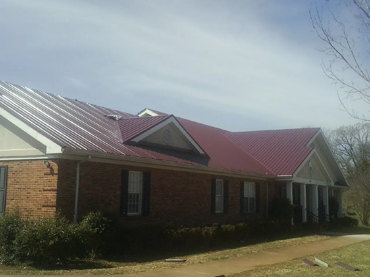 Red metal roof with gabled entries on a long brick building, from a Hail Damage Roof Repair job in Enid