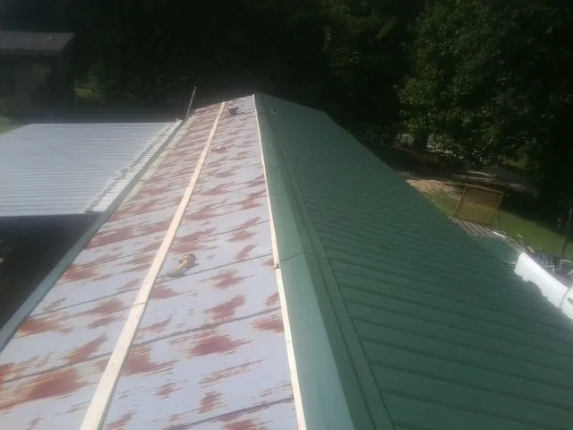 Old rusted panels beside newly installed green metal roofing — Wind Damage Roof Repair by Roofing Brothers in Enid