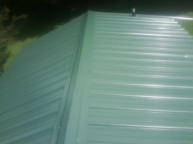 New green metal panels meeting at the ridge of a roof — Flat Roof Repair work by our crew in Enid