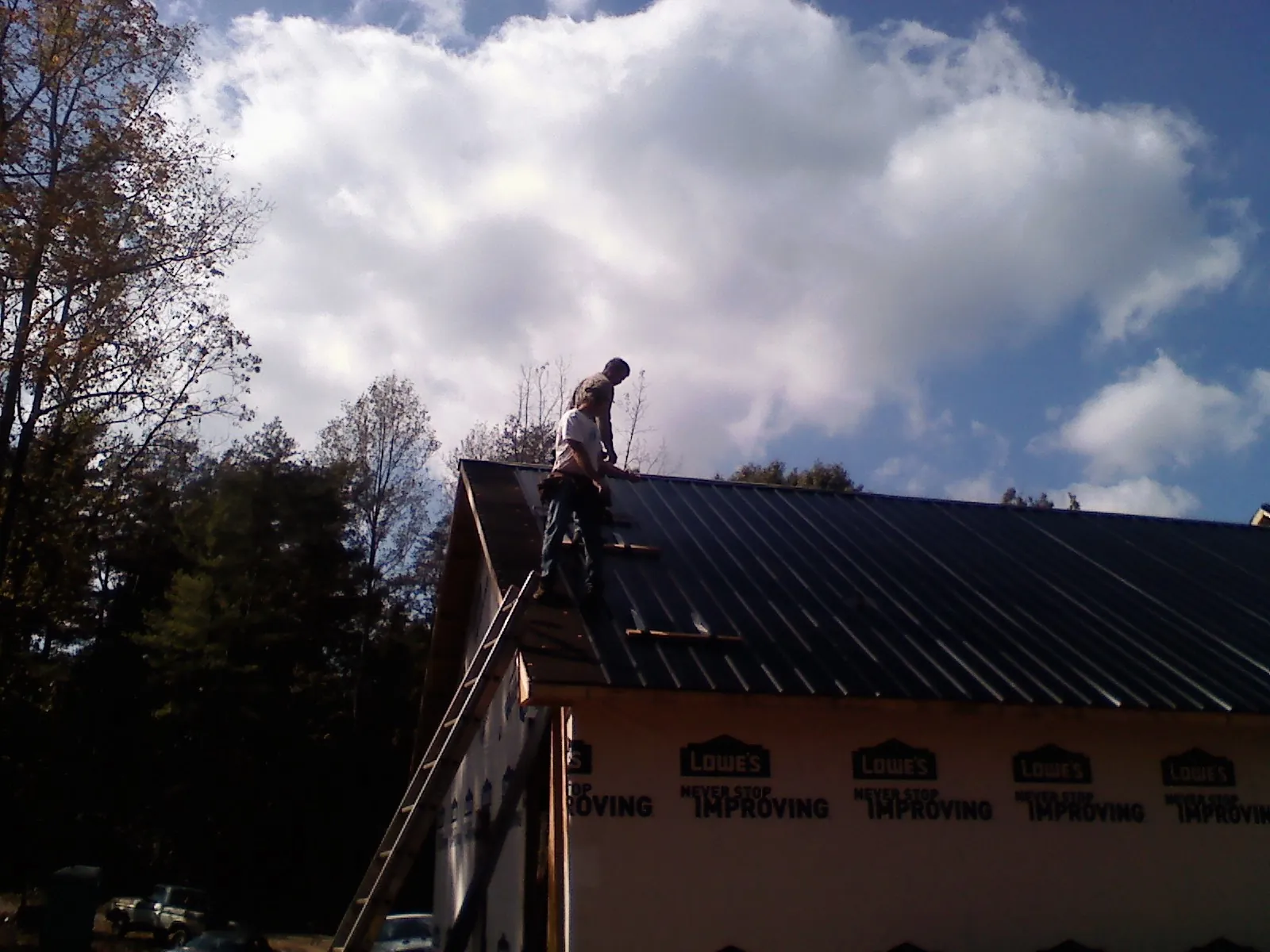 Roofer fastening dark metal panels high against a cloudy sky, from a Roof Inspection job in Enid