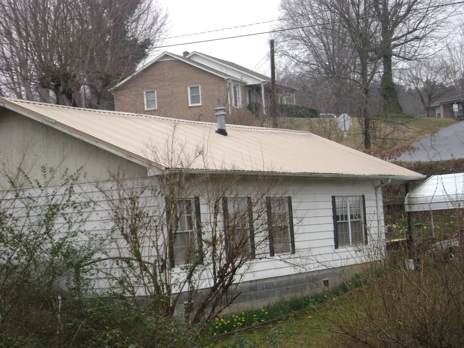 Tan metal roof on a white sided house set into a hillside — Commercial Roofing by Roofing Brothers in Enid