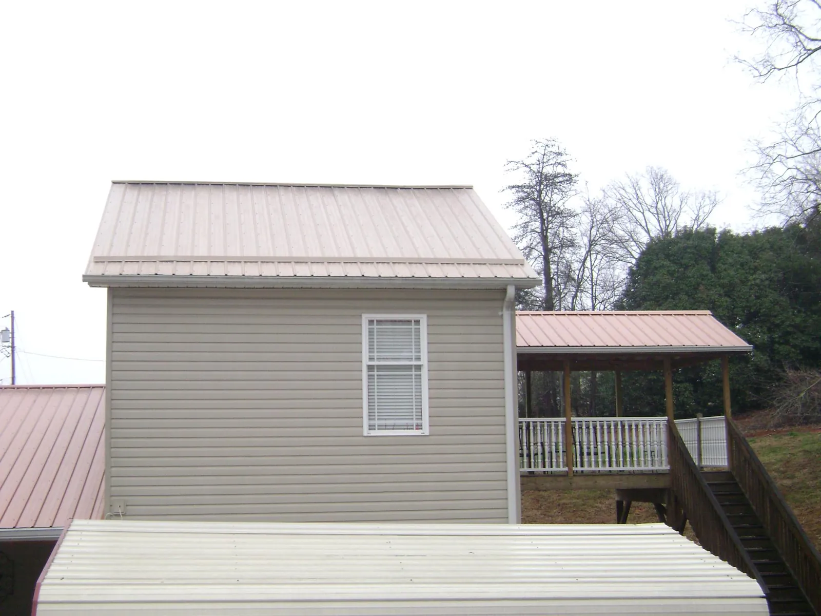 Tan metal roofs on a two story addition and attached porch, from a Roof Replacement job in Enid